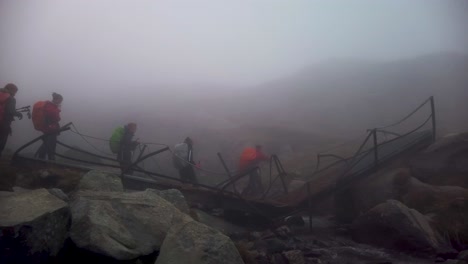 A-group-of-hikers-crossing-a-broken-bridge-on-a-foggy-mountain