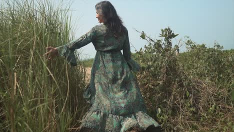 Slow-motion-medium-shot-of-pretty-woman-in-green-dress-walking-through-field-of-tall-grass-at-sunset