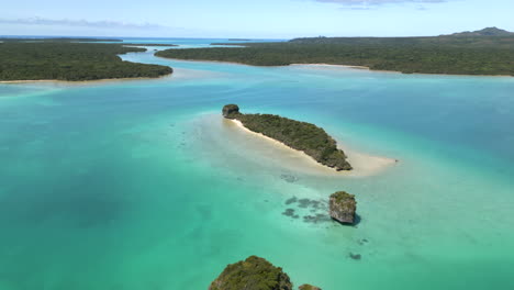 Upi-Bay,-Isle-of-Pines-and-islets-in-the-turquoise-water---pull-back-aerial-flyover