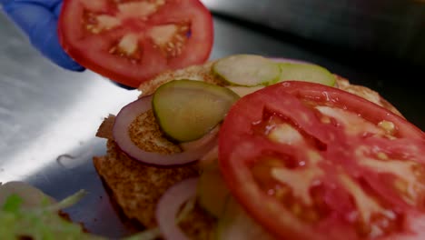 Tomato-slice-placed-on-burger-prepared-in-restaurant-kitchen,-close-up