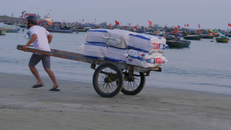 Tracking-shot-of-a-delivery-driver-running-with-a-hand-cart-carrying-the-goods-along-the-beach