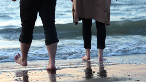 A-Couple-Walking-Barefooted-On-The-Shore-With-Rough-Waves