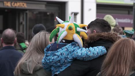 Gente-Esperando-El-Desfile-De-San-Patricio-En-La-Ciudad-De-Cork,-Un-Padre-Sosteniendo-A-Un-Niño-Con-Un-Sombrero-Colorido