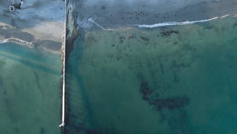 Green-blue-ocean-water-waves-crash-peacefully-on-sandy-shoreline-by-seawall