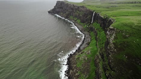 Waterfall-Pours-Down-Lush-Green-Cliff-Into-Ocean,-Talisker-Waterfall,-Scotland
