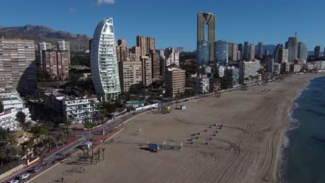 Aerial-flight-over-sandy-beach-in-Benidorm-with-modern-buildings-named-Delfin-and-Intempo-Tower-in-background