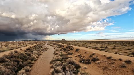 Mojave-Desert's-Cache-Creek-full-of-water-as-a-thunderstorm-gathers-on-the-horizon---aerial-flyover