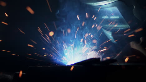 Sparks-fly-and-smoke-rises-in-slow-motion-as-a-welder-fuses-metal-in-a-workshop