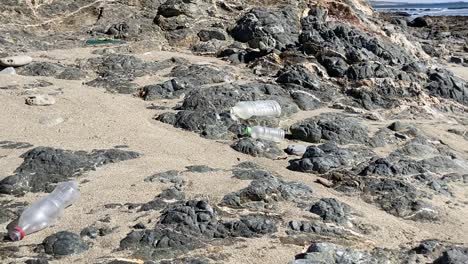 Plastic-marine-debris-littered-on-rocky-and-sandy-coastline-pan