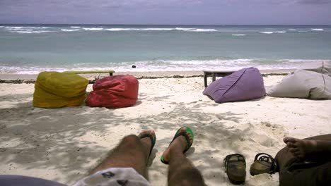 Male-lounges-beachside-on-bean-bag-in-shade-of-trees-on-sunny-windy-day