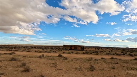 Abandoned-trailer-cabin-in-the-Mojave-Desert-by-Cache-Creek-full-of-muddy-water-after-a-storm---aerial-flyover