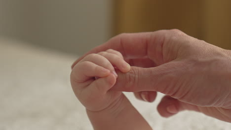 close-up-baby-hand-holding-mother-thumb,-massaging,-cuddling-in-bright-bedroom