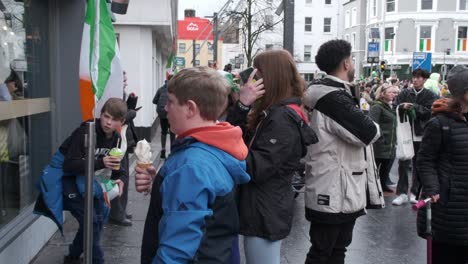 Bandera-Irlandesa-Y-Grupo-De-Adolescentes-Con-Multitud-Llenando-La-Calle-En-La-Ciudad-De-Cork-Durante-St