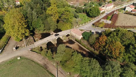 Car-Crossing-Roman-Bridge-in-Rural-Village-Aerial-View