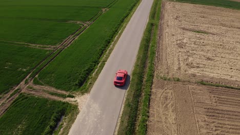 Cinematic-drone-shot-of-an-orange-Ford-Mustang-GT-driving-down-a-straight-road-surrounded-by-green-fields