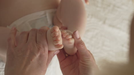 newborn-baby-feet-and-toes,-mom-massages-with-both-hands,-white-bedsheets