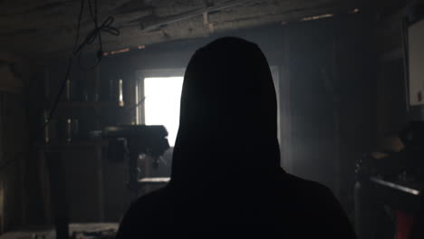 Hooded-person-walks-into-metal-workshop-from-behind