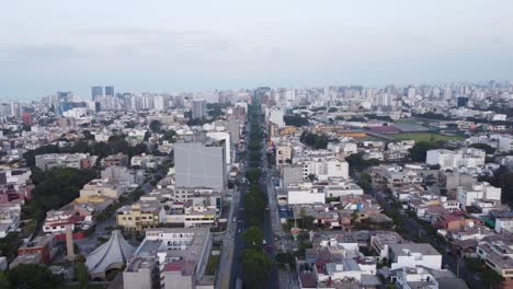 Drone-flying-forward-above-a-street-called-"Avenida-Benavides"-with-many-trees-in-the-middle-of-the-2-lanes,-going-into-the-distant-horizon-of-the-city