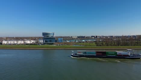 Inland-Ship-Carrying-Containers-With-Modern-Building-In-BackGround