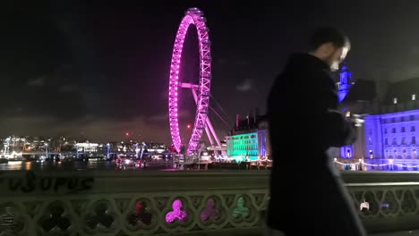 Zeitrafferaufnahme-Des-London-Eye-Von-Der-Westminster-Bridge-Bei-Nacht,-Während-Touristen-Und-Einheimische-Durch-Die-Aufnahme-Laufen