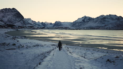 A-person-handling-a-tripod-is-going-on-the-beach-in-lofoten-islands-in-winter
