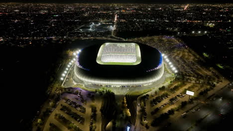 Aerial-view-tilting-towards-the-illuminated-BBVA-stadium,-nighttime-in-Monterrey,-Mexico