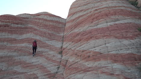 Female-Hiker-Walking-Uphill-on-Strange-Swirled-Layered-Sandstone-Patterns,-Slow-Motion