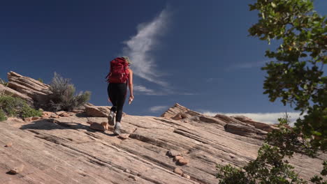 Back-of-Woman-With-Backpack-Walking-on-Rocky-Hill-in-Desert-Under-Blue-Sky,-Slow-Motion