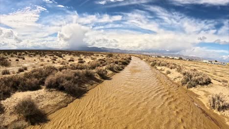 Usually-dry-riverbed-of-Cache-Creek-in-the-Mojave-Desert-flowing-with-water-after-a-rainstorm---aerial-flyover