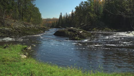Ein-Fluss,-Der-An-Einem-Schönen-Tag-Um-Eine-Felseninsel-Fließt,-Mit-Herbstfarben-Im-Hintergrund