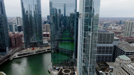 Green-colored,-dyed-river-mirroring-from-high-rise-windows-in-downtown-Chicago,-USA---Aerial-view