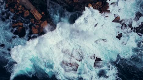 Drone-Ascends-from-Waves-Crashing-on-Rocks-in-Ocean,-Coogee-Beach