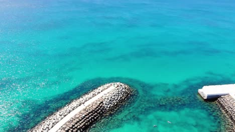 Aerial-View-Of-Idyllic-Blue-Ocean-Waters-With-Breakwater-Wall-Surrounding-Bikini-Beach-Club-At-Cape-Verde