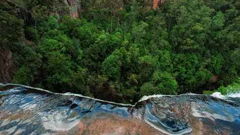 Belmore-Falls,-Australia,-Drone-Slowly-Pans-Down-over-Waterfall-Edge