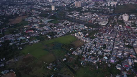 Suburb-of-Ho-Chi-Minh-City,-Vietnam-with-rice-field,-residential-area-main-road-and-urban-sprawl-as-seen-from-aerial-view-on-sunny-afternoon