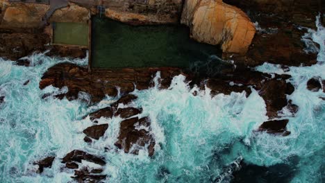 Descending-Drone-of-Blue-Waves-Crashing-at-Bermagui-Blue-Pool,-Australia