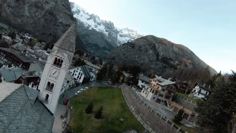 FPV-drone-aerial-past-church-in-alpine-mountain-resort-centre-of-Courmayeur,-Aosta-Valley,-Italy,-Mont-Blanc-Monte-Bianco,-flying-over-houses