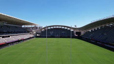 Vista-Aérea-Del-Estadio-De-Rugby-Pasando-Por-Postes-De-Gol,-Gradas-Y-Campo-De-Hierba