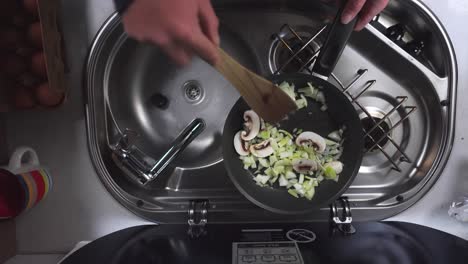 Top-down-shot-of-a-man's-hands-stirring-vegetables-with-a-cooker-on-a-small-stove-in-a-caravan