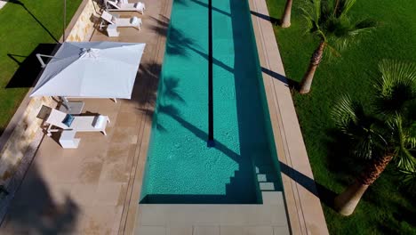 Luftaufnahme-Des-Pools-Einer-Luxuriösen-Villa-Mit-Palmen-Und-Sonnenschirmen,-Umgeben-Von-üppigem-Rasen