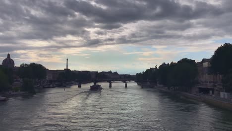 A-stunning-slow-motion-captures-the-beauty-of-France's-Seine-river-as-a-boat-gliding-along-the-waters-and-flows-gently-through-Paris,-with-trees-on-both-banks-it,-and-gray-cloudy-and-blue-sky