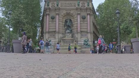 A-slow-motion-shot-of-the-Fontaine-Saint-Michel-in-the-streets-of-Paris,-with-people-walking-around