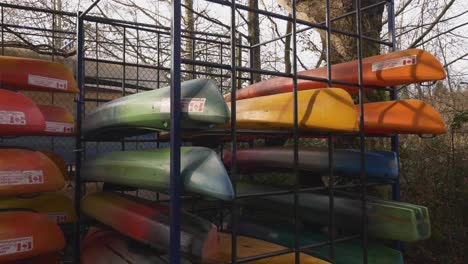 colorful-Canoes-with-canadian-flag-sticker-stored-stacked-organized-behind-a-locked-fence-during-autumn-fall-off-season-at-public-park-facility