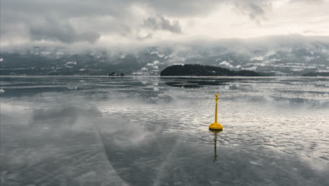 Gelbe-Sondermarkierungsboje-Auf-Dem-Zugefrorenen-Steinsfjorden-See-Mit-Wolken-In-Norwegen