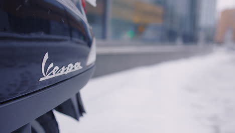 Close-up-of-Vespa-logo-on-back-of-vehicle-on-snowy-winter-day