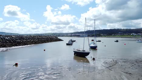Aerial-view-moored-boats-on-Welsh-low-tide-seaside-breakwater-harbour-coastline-low-pull-away-left
