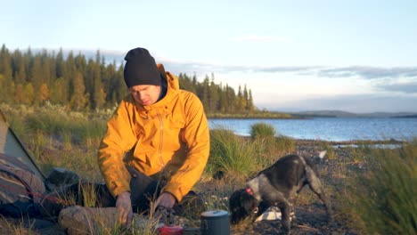 Maverick-Camper-man-and-his-dog-at-lakeside-campsite-in-wild-Sweden---Push-in-Wide-slow-motion-shot