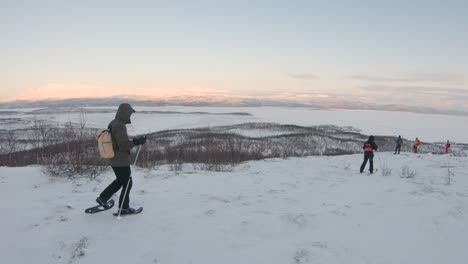 Hiker-with-snowshoes-and-poles-walking-on-a-mountain-during-sunrise-in-the-nature-in-northern-Sweden