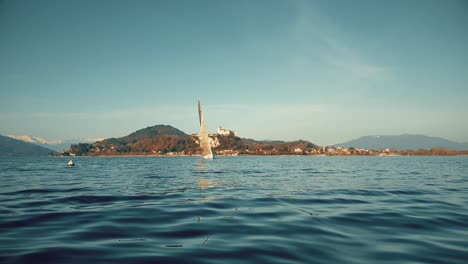 Low-angle-pov-of-bow-of-boat-sailing-on-Maggiore-lake-with-castle-in-background