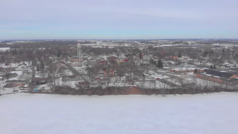 Circling-drone-aerial-shot-over-a-frozen-lake-and-small-midwest-town-in-the-winter